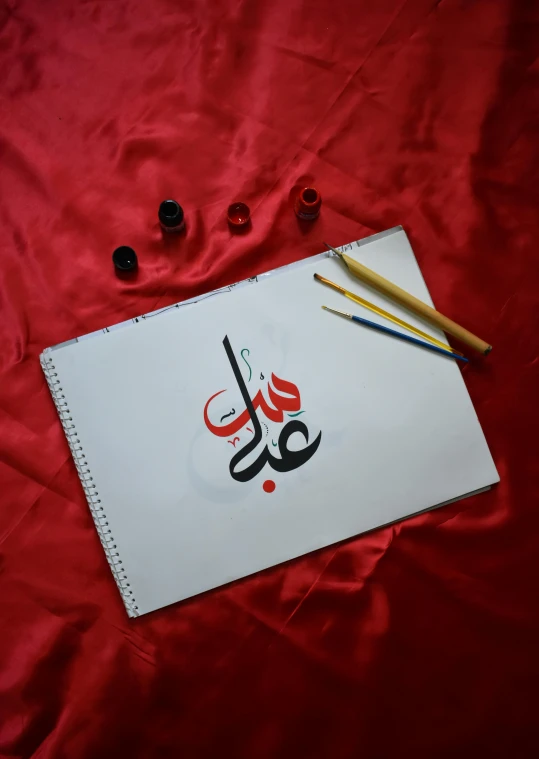 pencils and paintbrush sitting on a sheet that is on top of red cloth