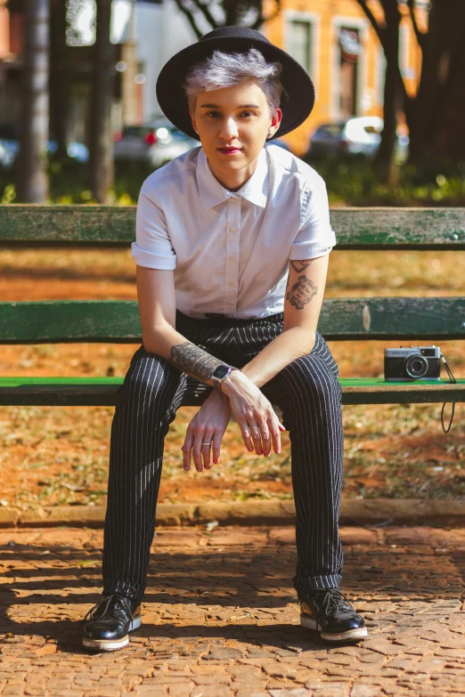 a young man with a large tattoo wearing a hat is sitting on a park bench