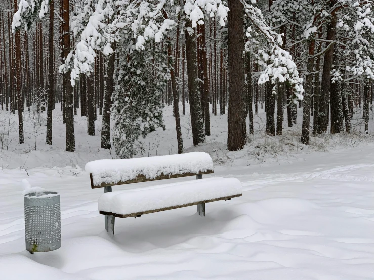 there is snow on the bench next to a trash can