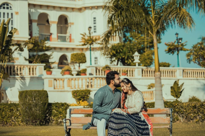 a couple poses on a bench in front of a large house