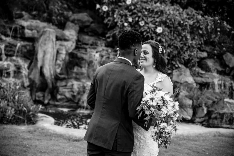 a bride and groom standing close together in the grass