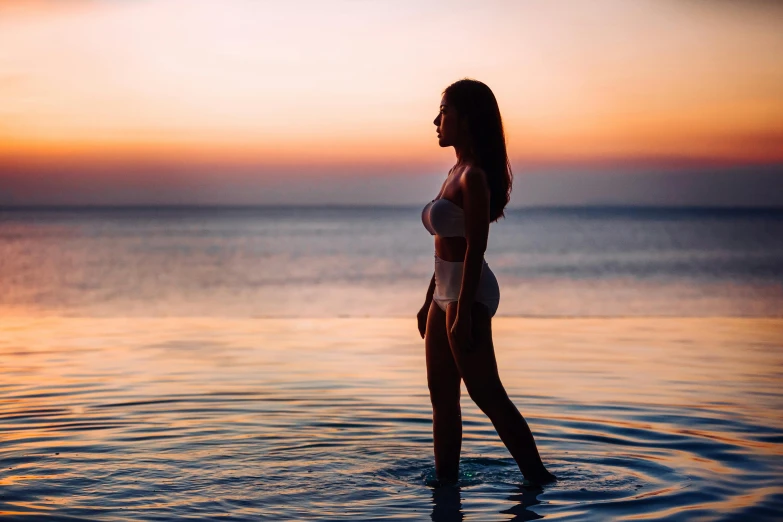 woman standing in water with pink sunset sky