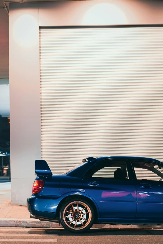 the rear end of a blue, coupe car in front of a closed garage door