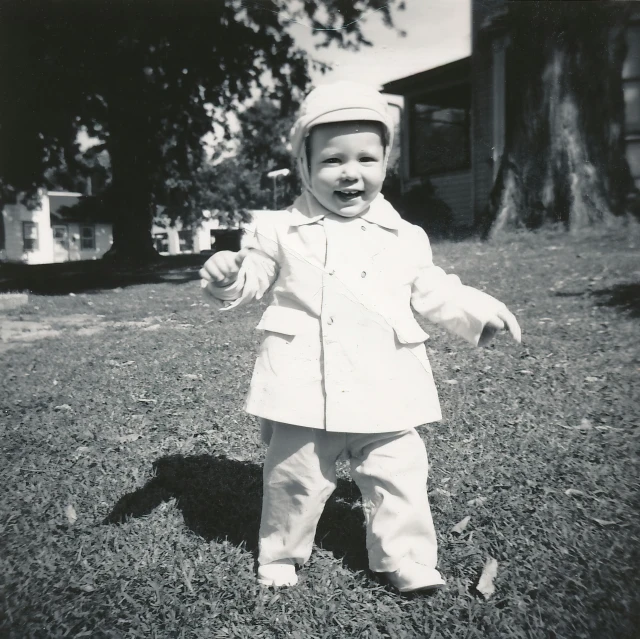 a baby in a white suit standing on top of grass