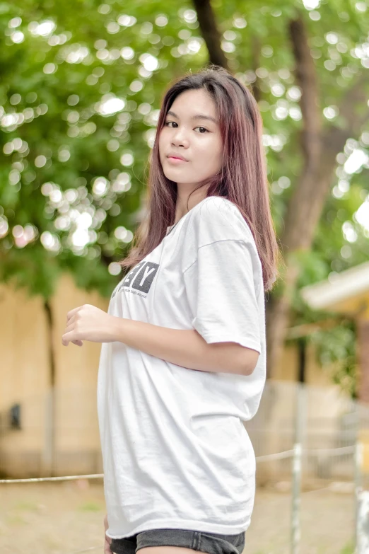 a young asian girl in shorts and a t - shirt standing near a tree