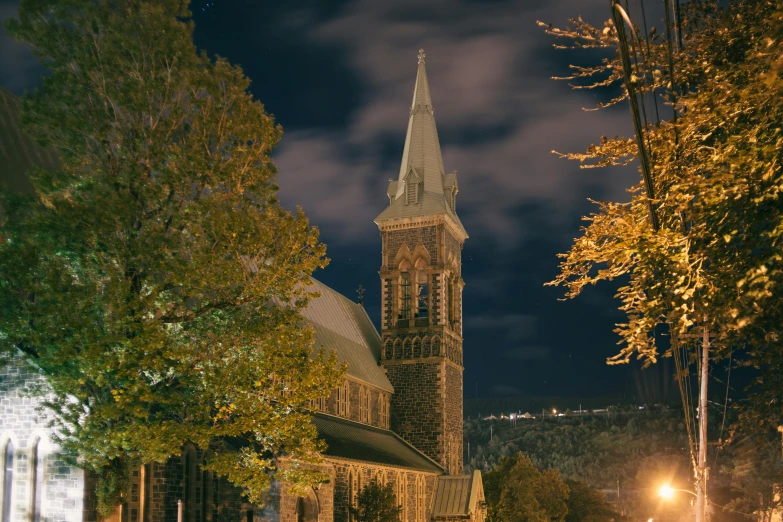 large stone church with spire and trees around