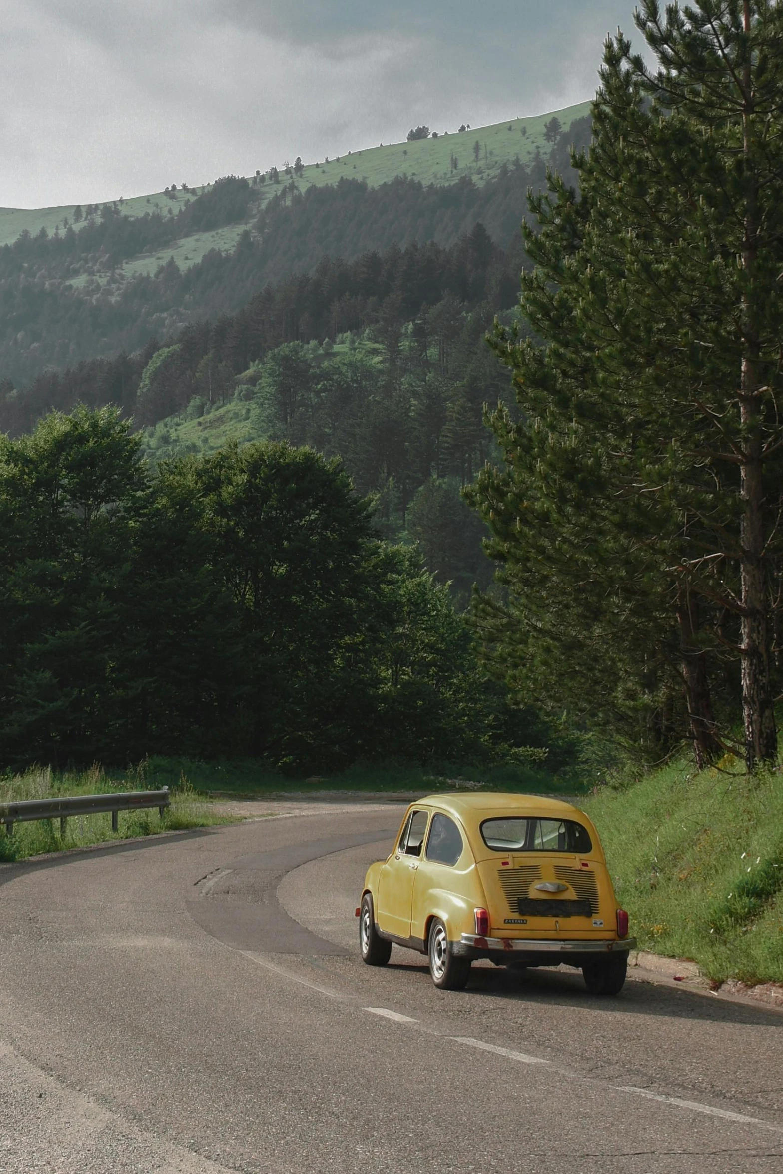 a small yellow car driving down a road with mountains behind it