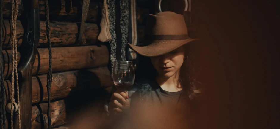 a young woman wearing a cowboy hat is holding a glass of wine
