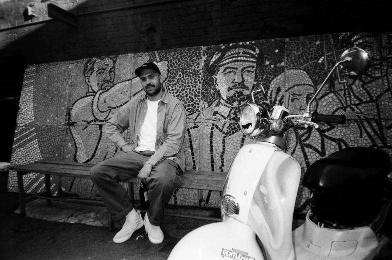 a man is sitting down on a park bench next to two scooters