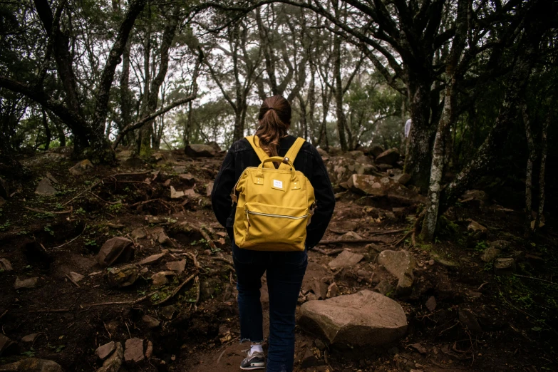 woman walking on trail with yellow backpack in wooded area