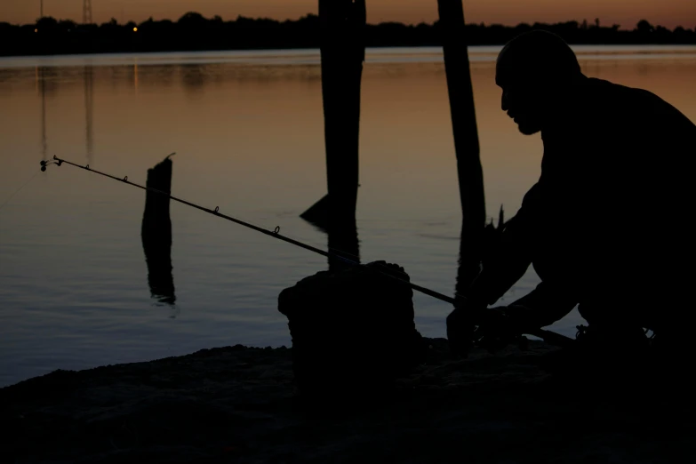 a man fishing at a lake with the sun setting