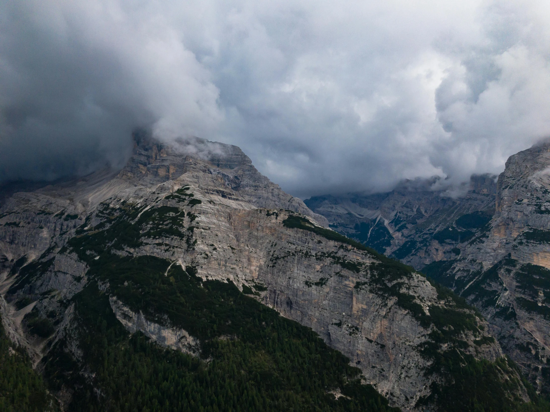 a mountain range with trees below it and the clouds above