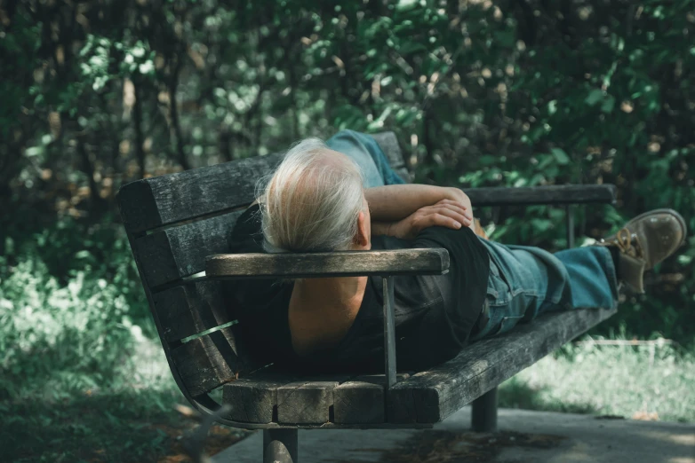 an old man laying on a bench in the woods