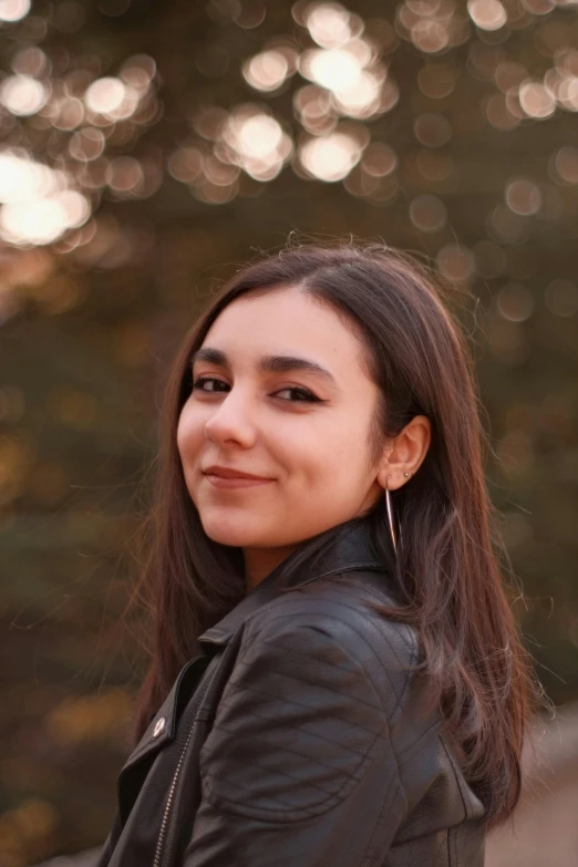 a pretty young lady standing in front of some trees