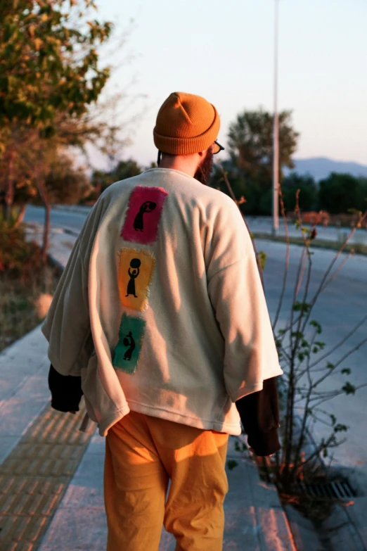 a man walking on a sidewalk while wearing a colorful sweatshirt and hat