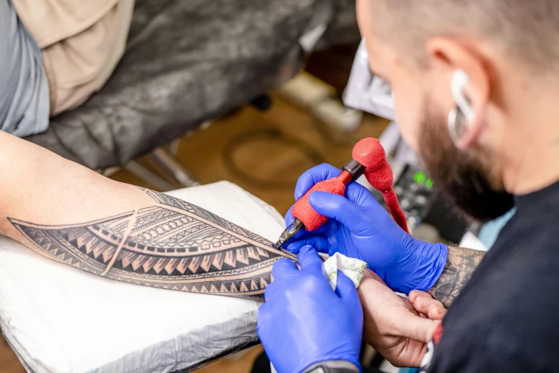 a man getting his arm tattooed while another is sitting