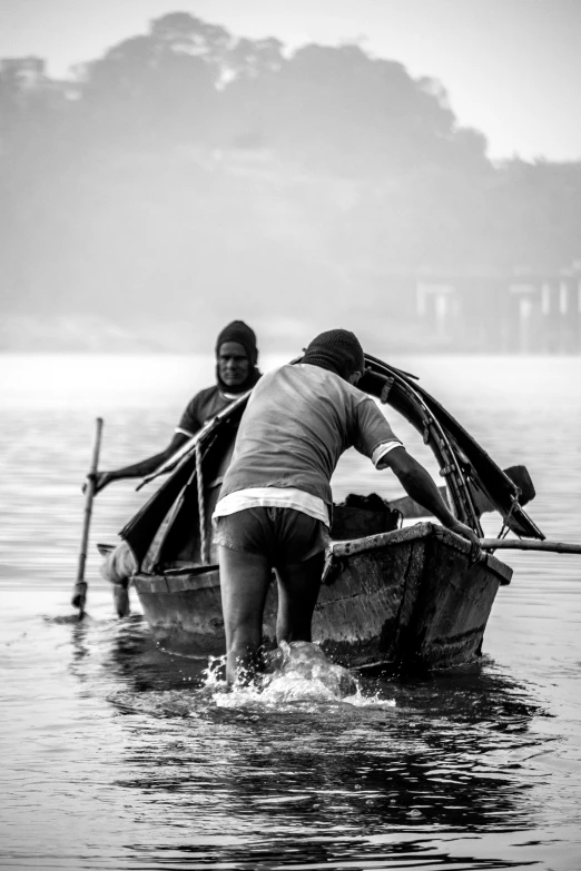 two men standing in the water rowing a boat