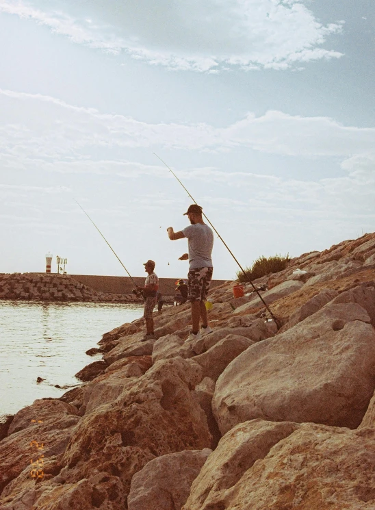 a man on rocks in front of water with fishing rods