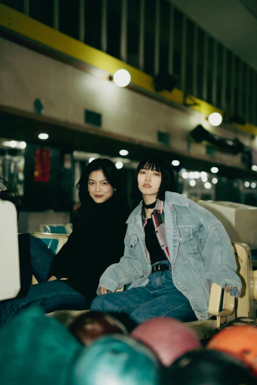 two young women sitting on top of a table near a pile of bowling balls