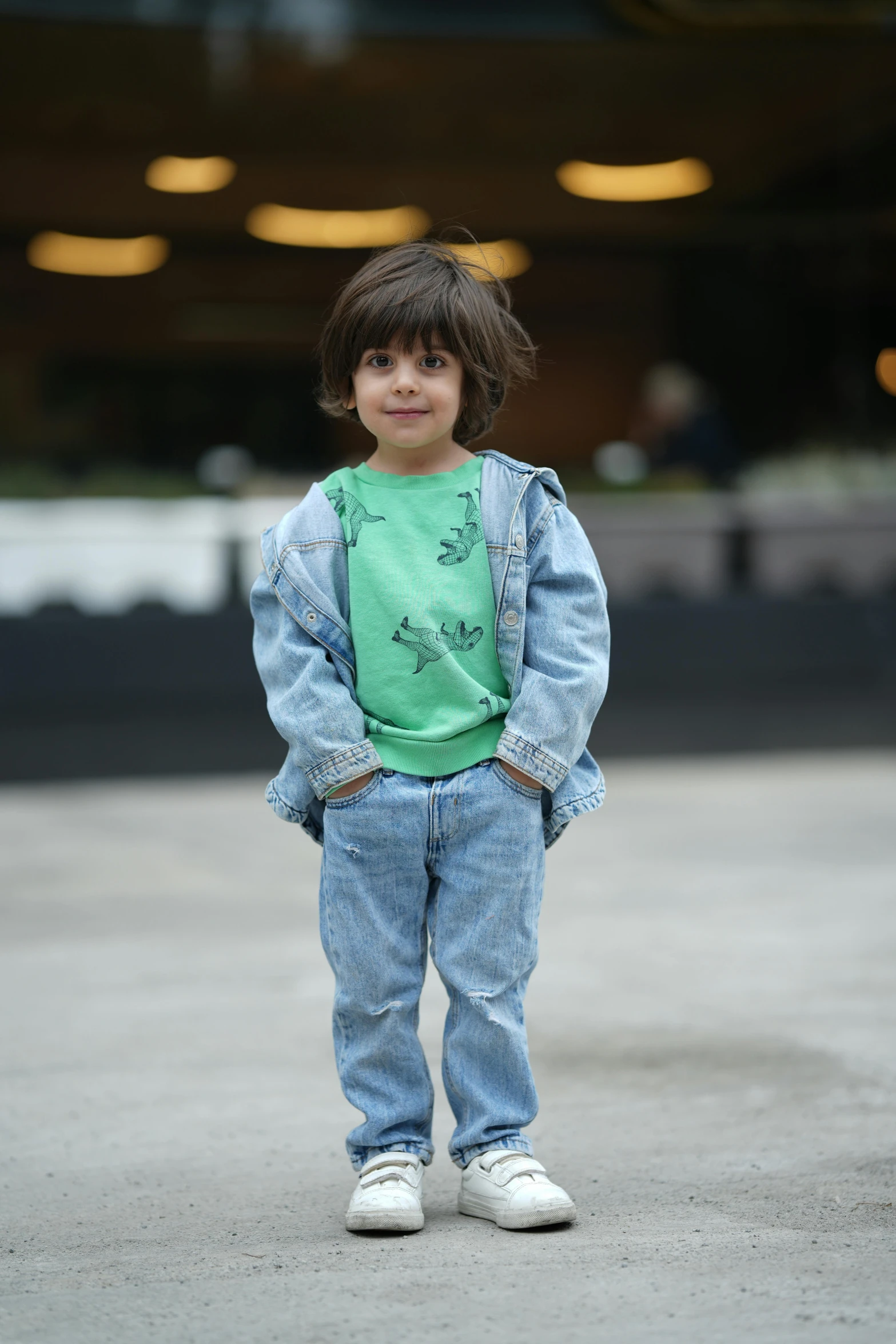 a little boy in overalls standing on concrete