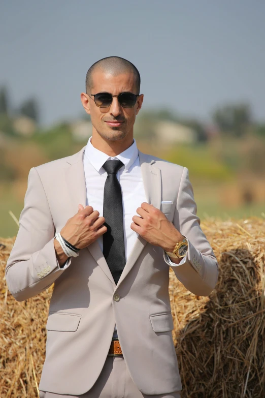 a man adjusting his tie in front of some hay