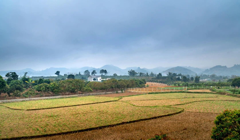 a landscape with green grass and a farm on a cloudy day