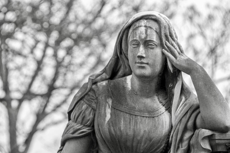 a statue stands outside with its hands near her face