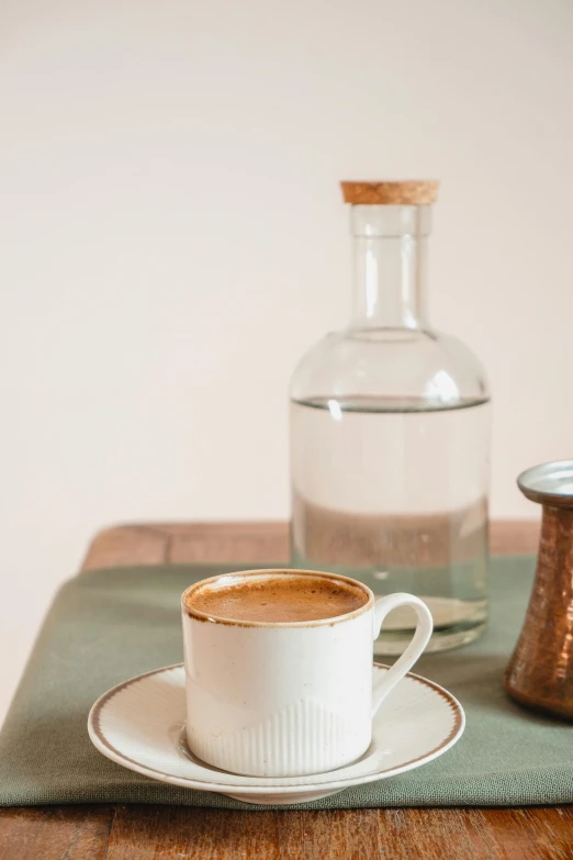 a cup of coffee on a saucer with a jug behind it