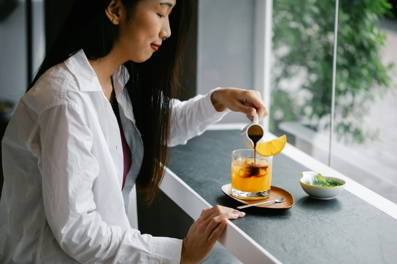 a woman is sitting at a counter and squeezing tea from a mug