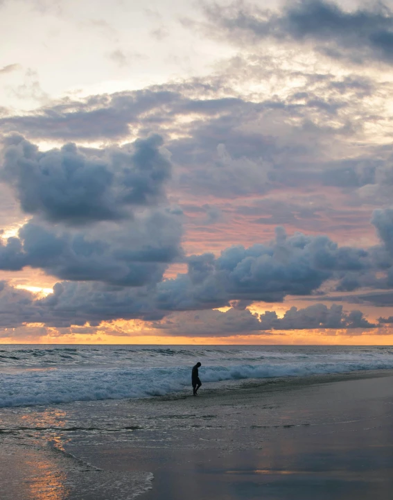 a person walking on a beach during a cloudy sunset