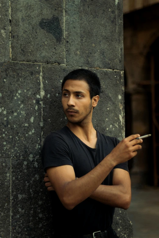 man leaning against pillar while holding cigarette in his hand