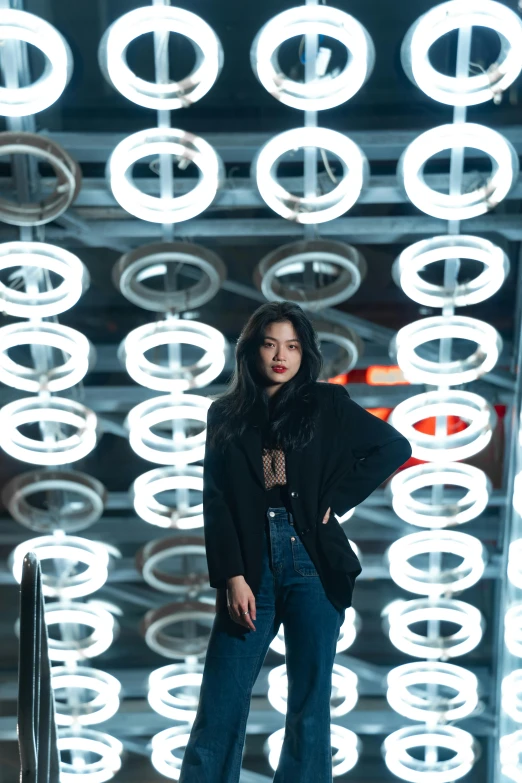 a woman in jeans and a jacket stands against a backdrop of circular lights