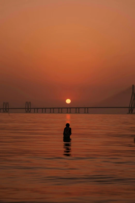 a man standing in the water at sunset