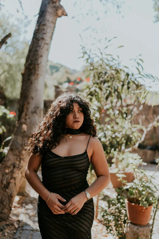 a woman poses against a tree in a black dress