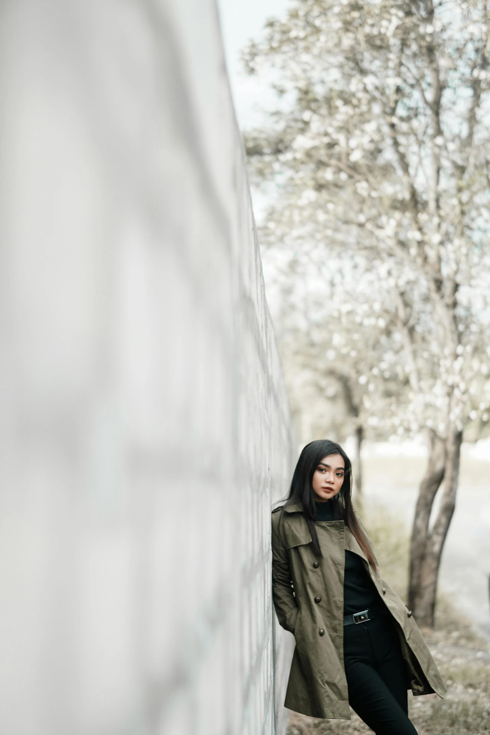 a woman leaning against a wall in a trench coat