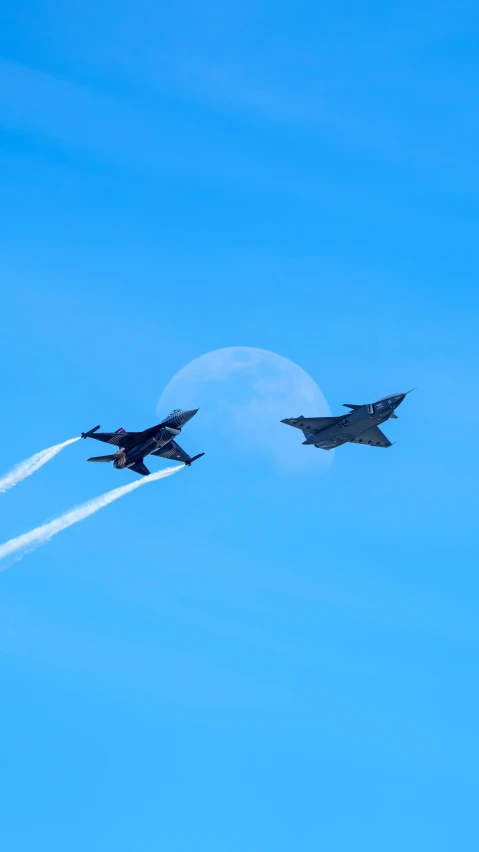 two fighter jets flying together under a moon