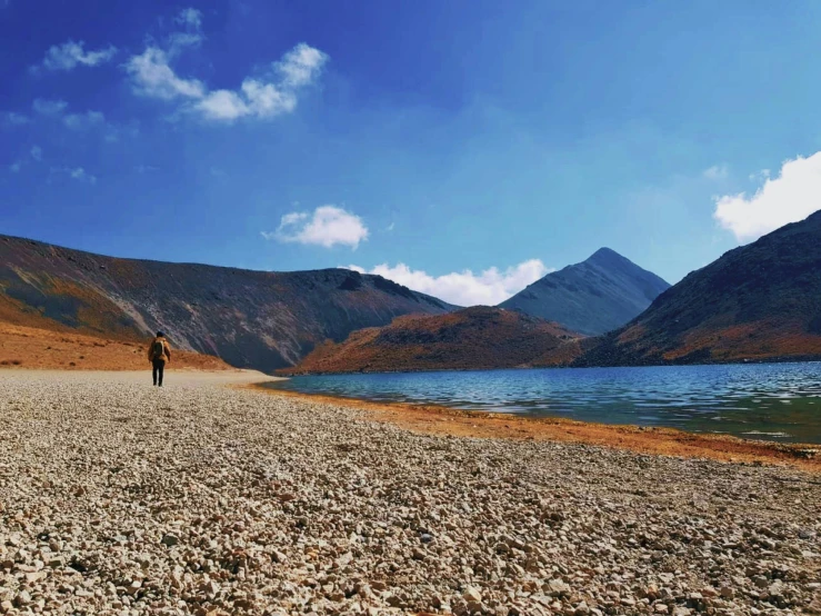 a lone person stands on the shores of a mountain lake