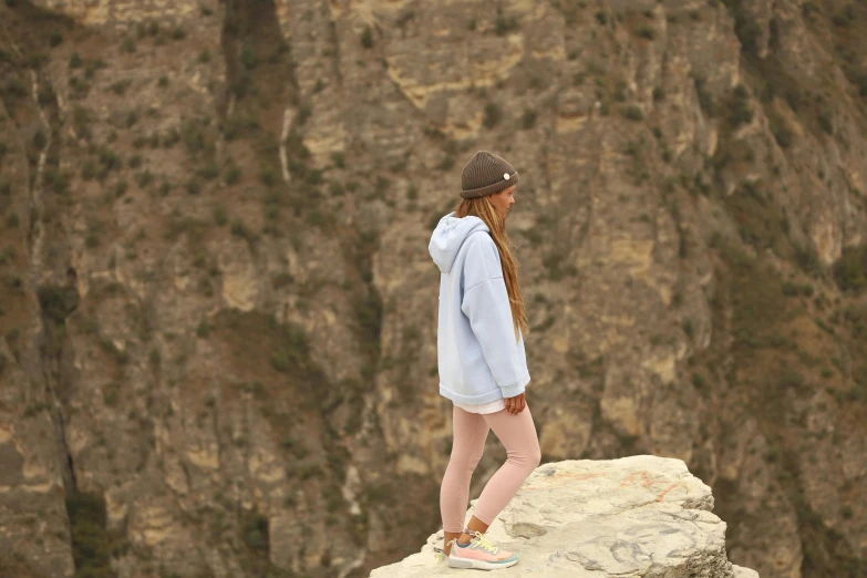 woman in shorts and a blue sweatshirt looks out at the cliff below