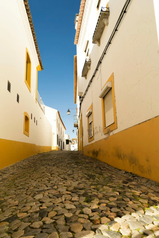 narrow cobblestone street with white houses and yellow shutters