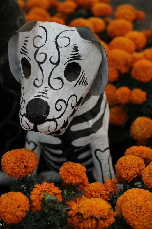 a statue of a dog made out of white and black sugar skulls sitting in some orange flowers