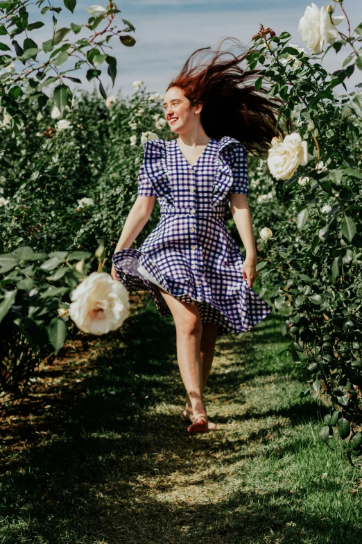 young lady in a purple gingham dress runs down a path near flowers