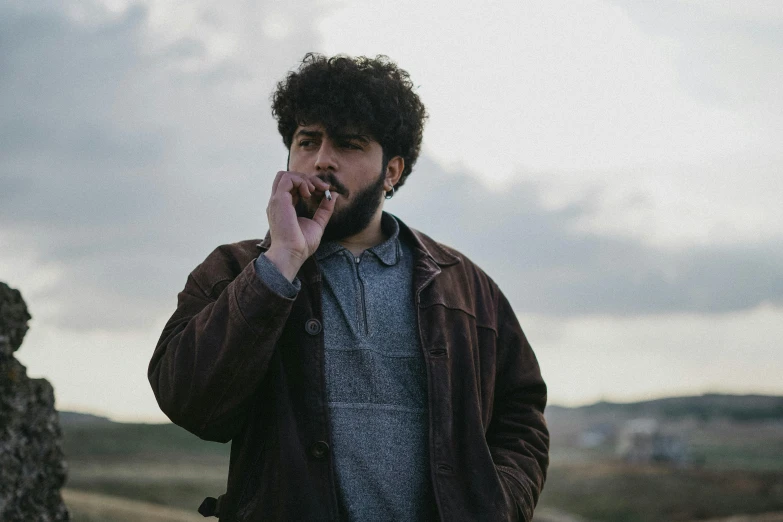 a young man smoking a cigarette and leaning against a rock wall