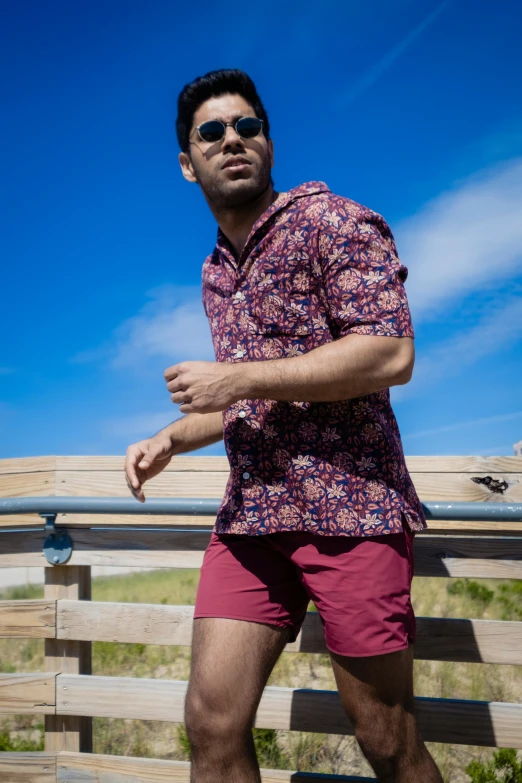 a man is wearing pink shorts and standing in front of wooden fence