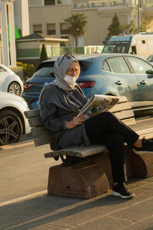 a person with a headscarf sits on a bench in the middle of a parking lot