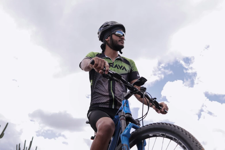 a man standing next to a blue bike under cloudy skies