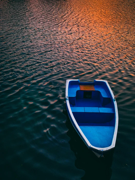 small boat sitting in the middle of a lake at sunset