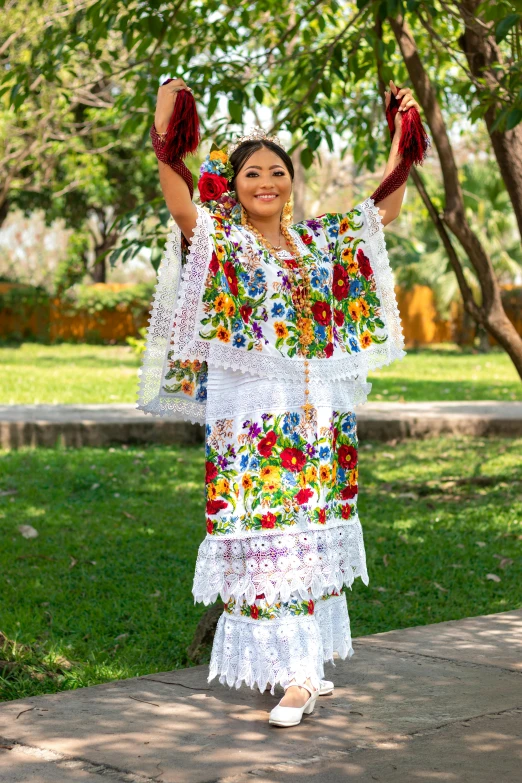 a woman wearing a colorful mexican dress stands on a sidewalk and holds her arms aloft