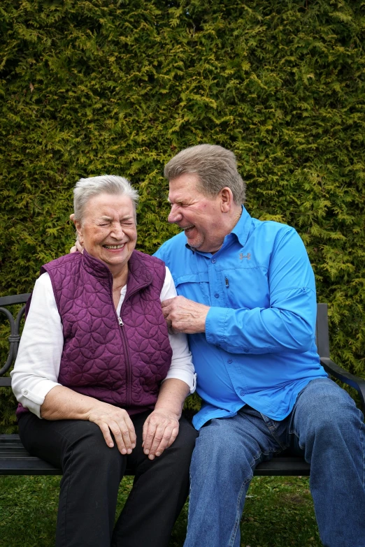 an elderly couple smiling and sitting on a bench