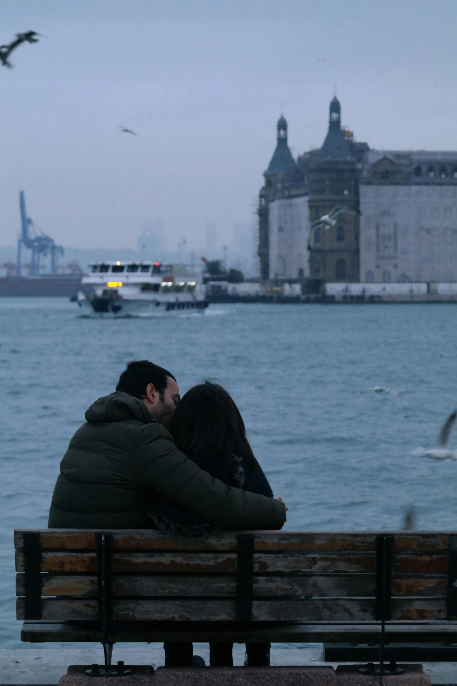 a man and woman are sitting on a bench overlooking the water