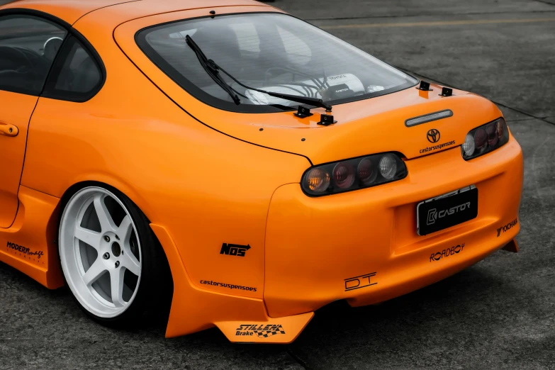 an orange sports car with white rims parked in a parking lot